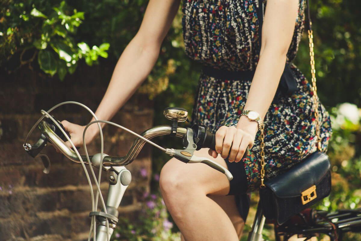 A closeup of a woman in a black floral dress riding a silver bicycle with a black purse