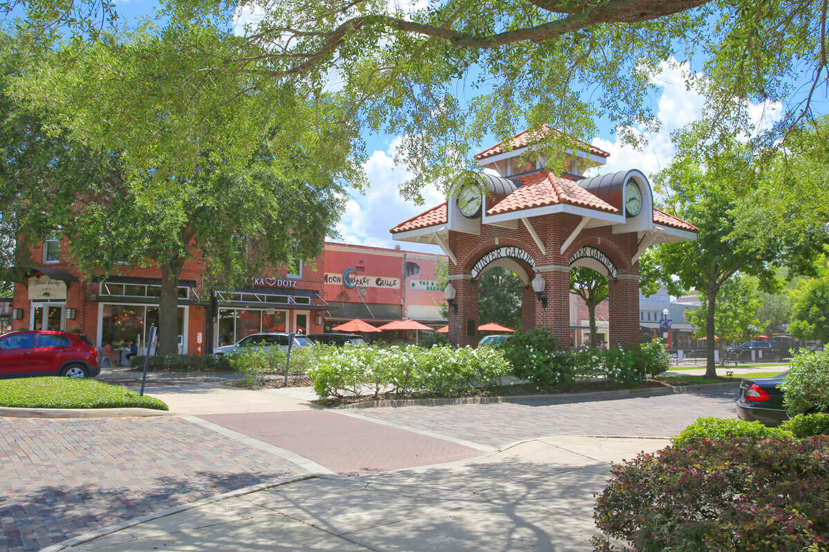 A brick road in front of a gazebo and a strip of shops and restaurants all surrounded by trees