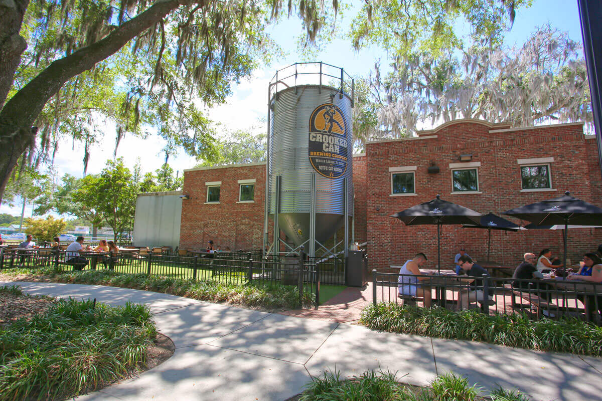 Exterior image of a brick brewery Crooked Can with people sitting at tables under umbrellas